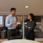 Zak and Sara collaborating inside a UK contact‑centre environment, mid‑discussion, with Zak lightly gesturing.