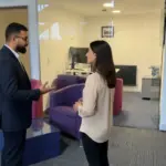 Omar and Sara discussing work inside a UK office background, engaged in a natural mid‑conversation moment.