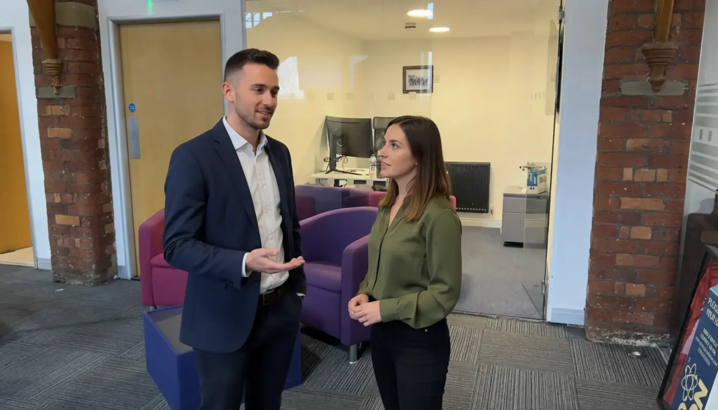 Adam and Jessica discussing CRM workflow improvements inside a UK office, engaged in mid-conversation.