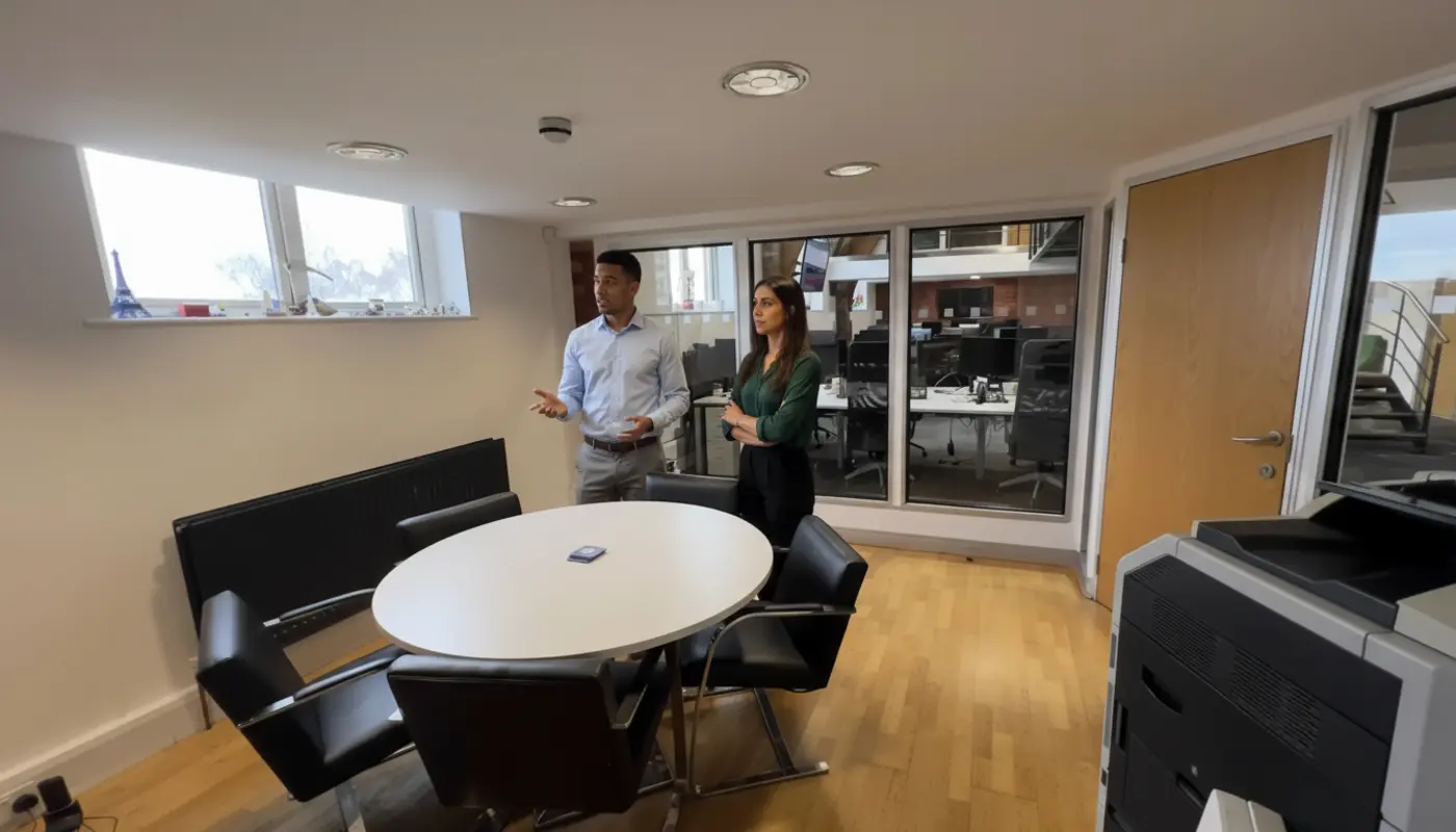 Zak and Sara discussing work inside a UK office, mid-conversation.