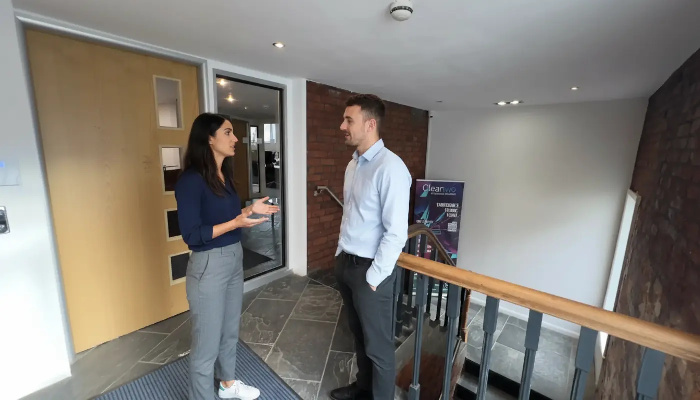 Sara and Adam conversing professionally in a UK office during a collaborative work moment.