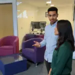 Zak and Sara discussing email marketing costs in a UK office environment, captured mid-discussion.