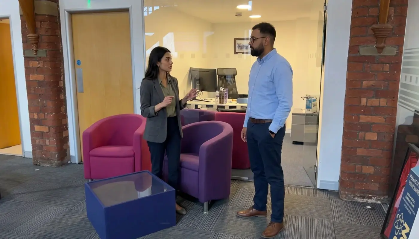 Two professionals discuss campaign delivery in a modern office while reviewing the next stage of work.