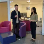Two colleagues discuss an email campaign plan in a modern office while reviewing strategy together.