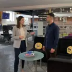 Jessica and Adam discuss early e‑commerce planning while standing in an open area of a UK office.