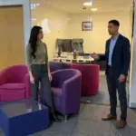 Two professionals discuss brand strategy in a modern office while standing apart in an open workspace.