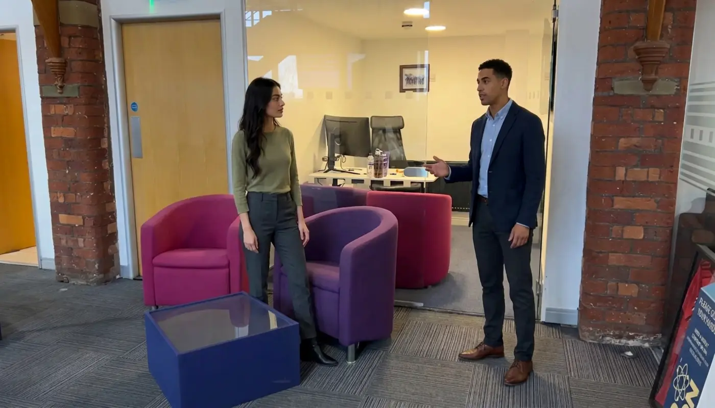 Two professionals discuss brand strategy in a modern office while standing apart in an open workspace.