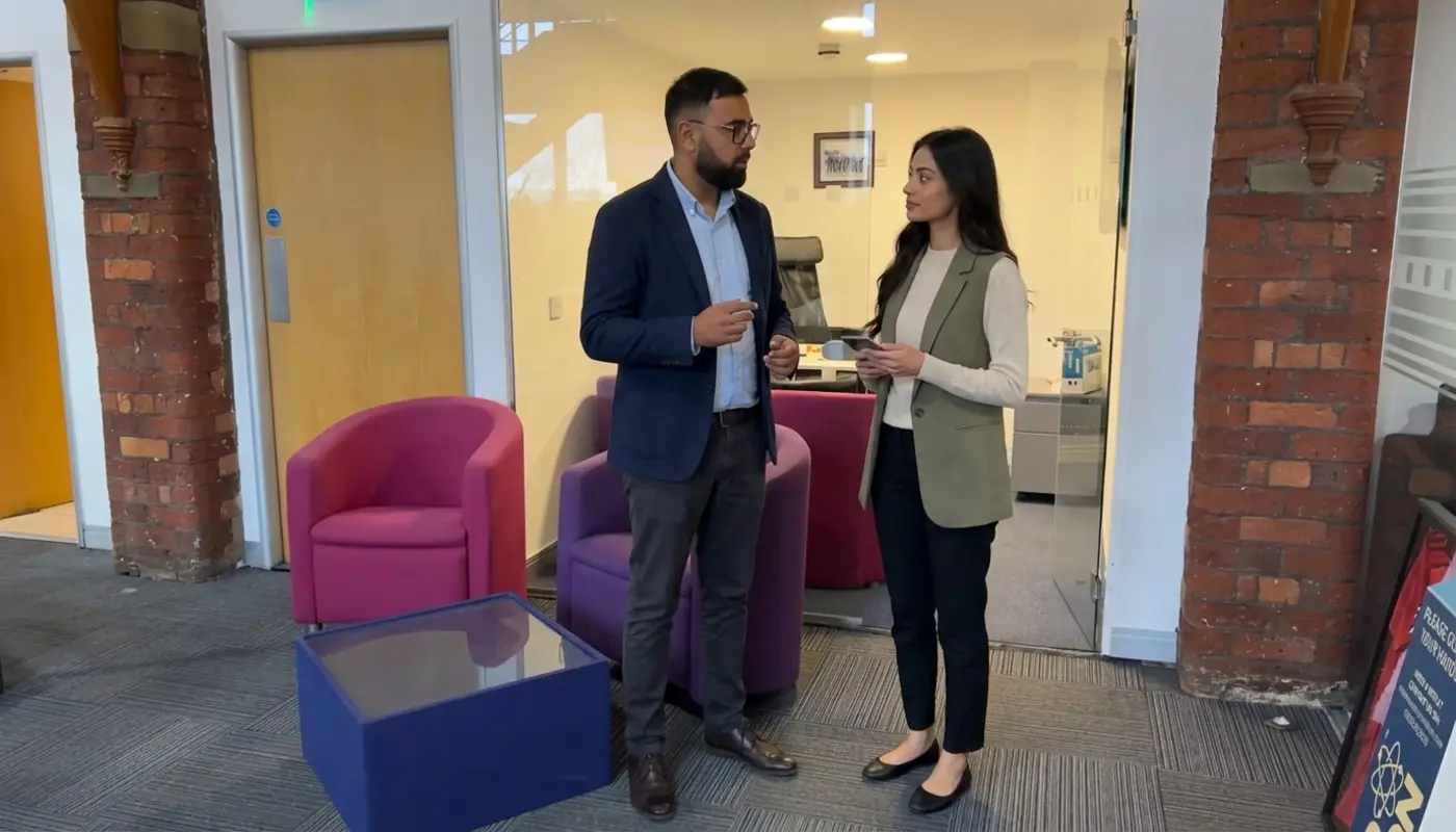 Two colleagues discuss a beginner social commerce setup in a UK office while checking an unreadable phone.