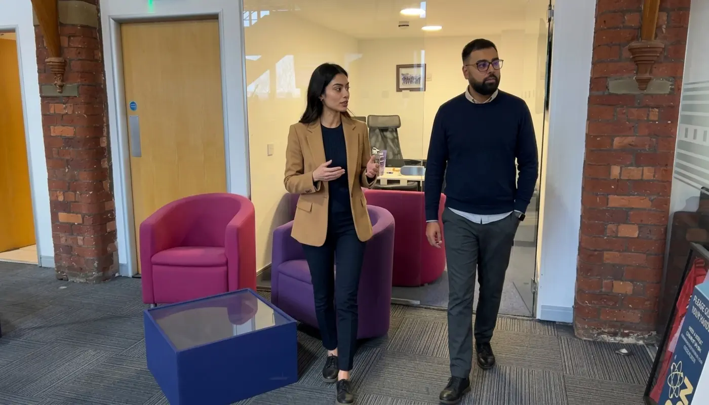 Two professionals walk through a modern office while discussing social campaign planning and goals.