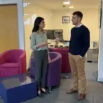 Two colleagues discuss an ecommerce shopping journey while standing in a modern office setting.