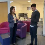 Two colleagues discuss everyday AI on a phone while standing in a UK office.