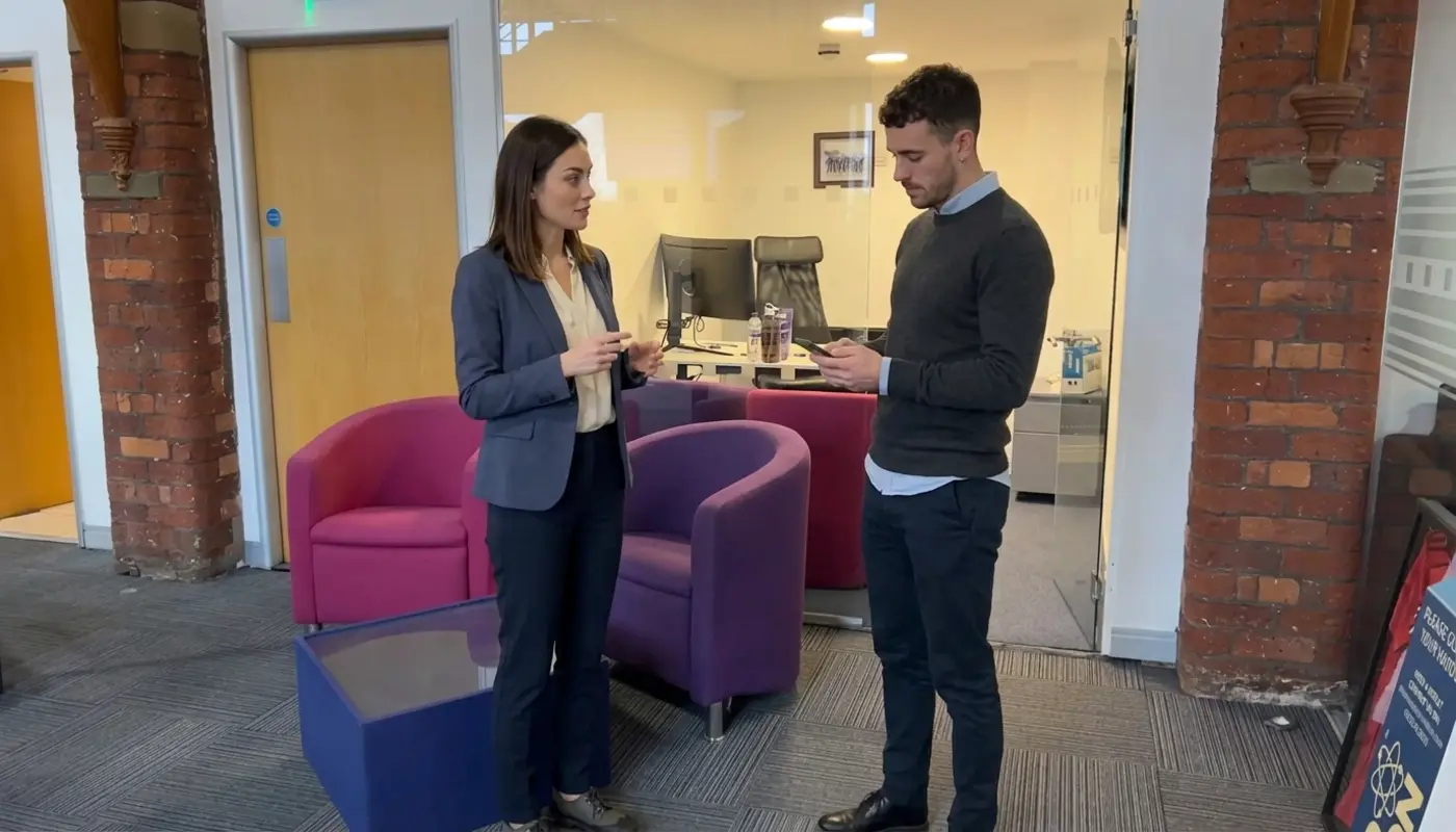 Two colleagues discuss everyday AI on a phone while standing in a UK office.