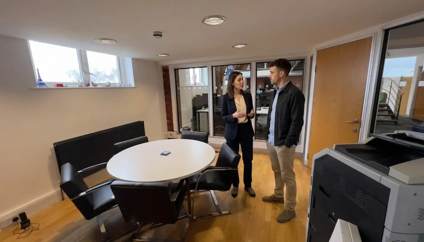 Two colleagues discuss paid social budget planning in a UK office during a professional conversation.