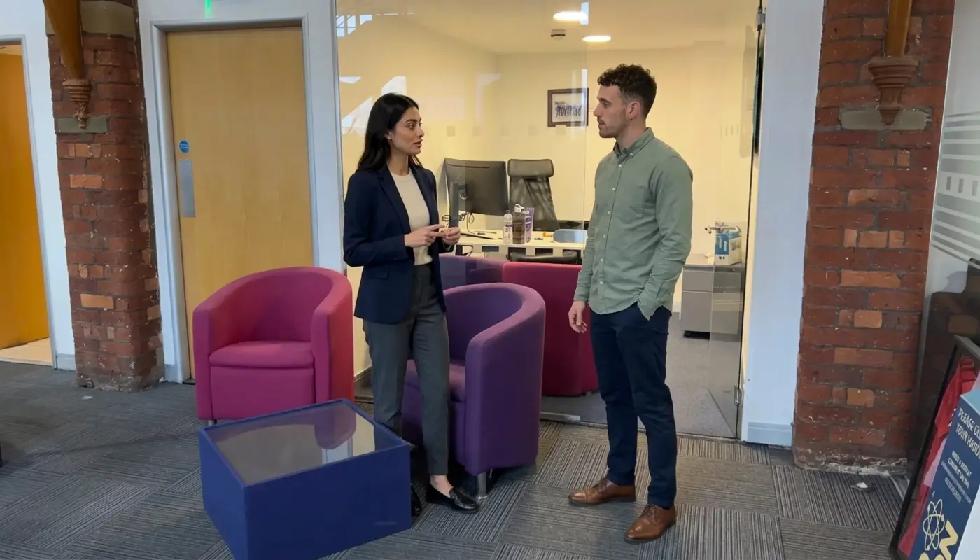 Two colleagues discuss ecommerce project scope in a UK office during a budget planning conversation.