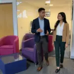 Two colleagues discuss CRM workflow needs while walking through a modern office.