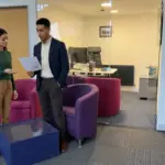 Two colleagues discuss rough logo ideas in a UK office during a brand identity planning session.