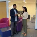 Two colleagues plan a TikTok Shop live run-through in an office while checking a phone setup.