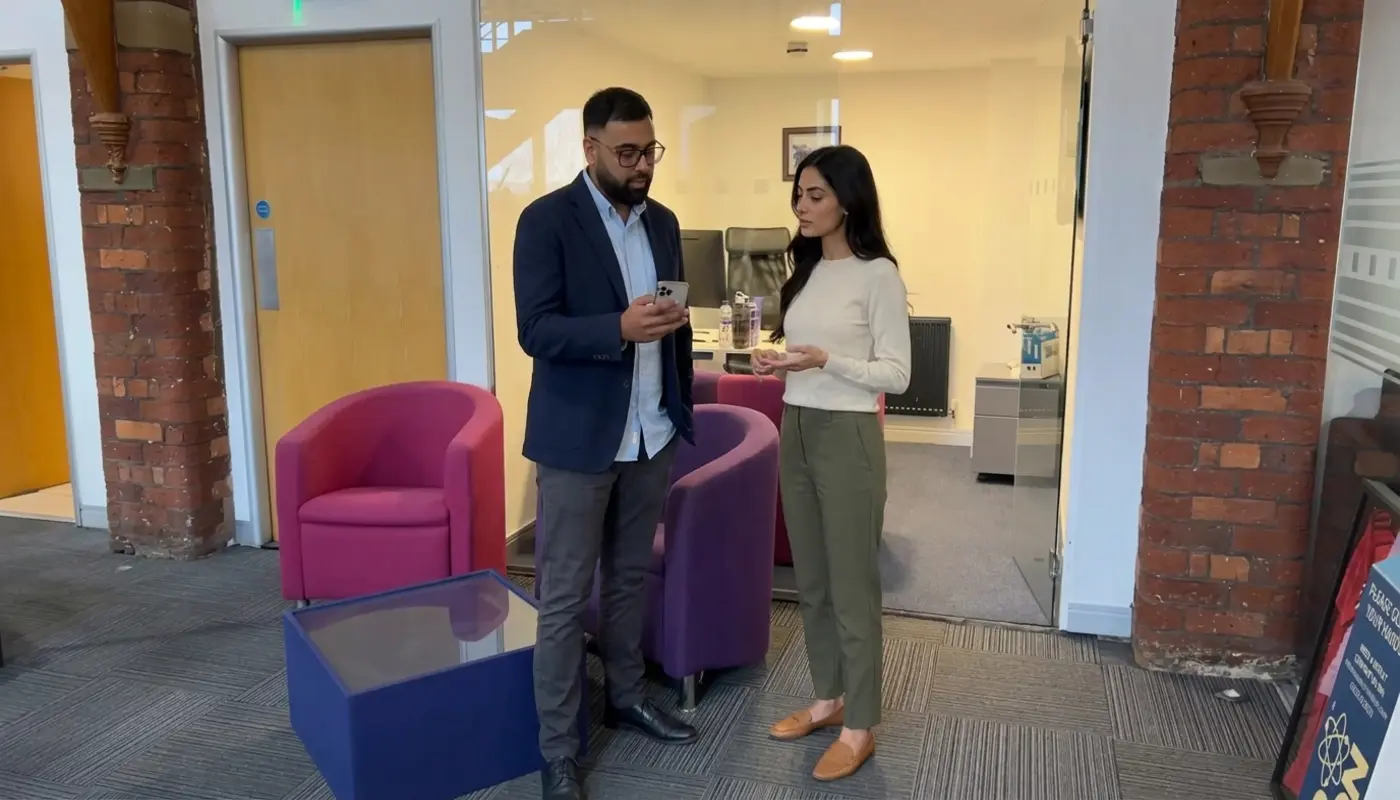 Two colleagues plan a TikTok Shop live run-through in an office while checking a phone setup.