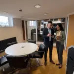 Two colleagues discuss an Instagram engagement workflow in a UK office while reviewing a phone together.