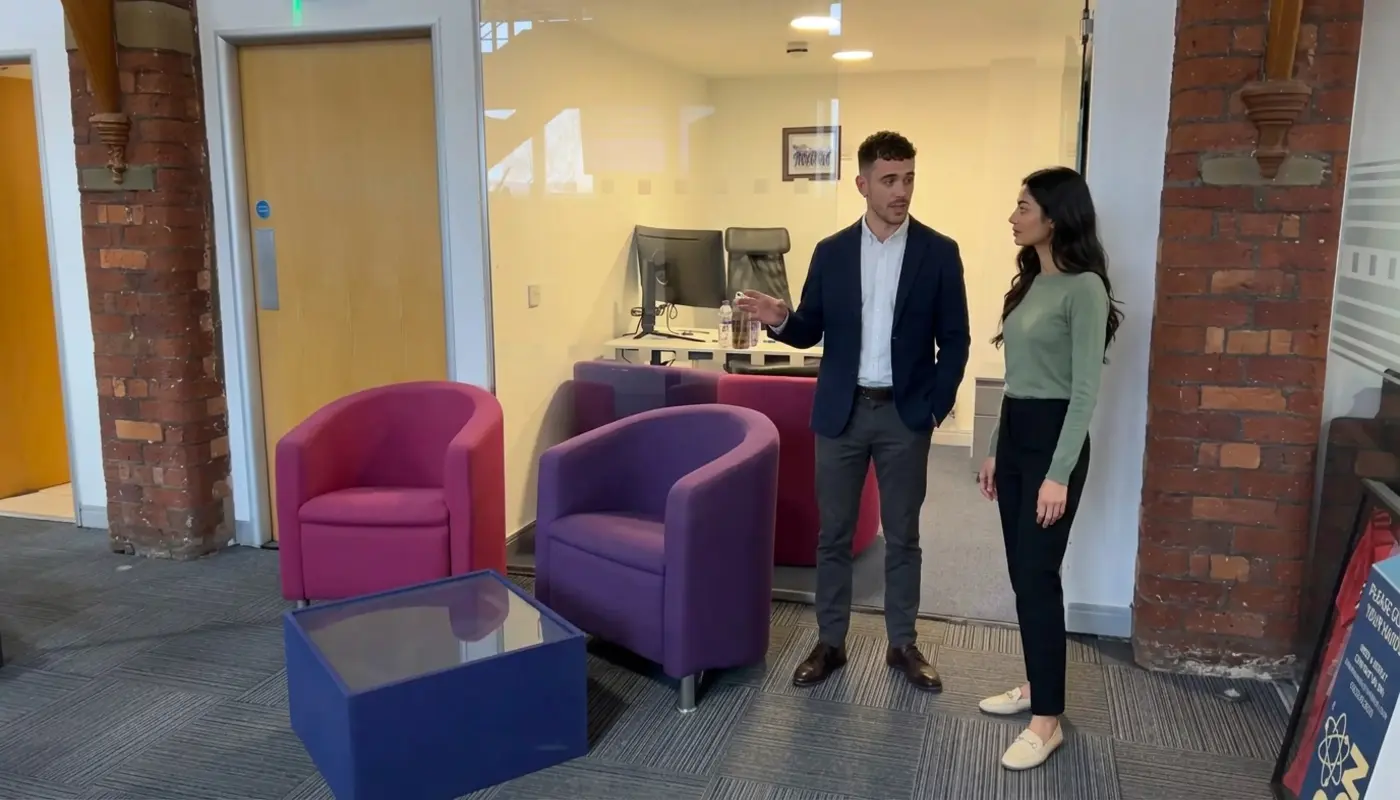 Two colleagues discuss CRM workflow in a UK office while standing in open floor space.