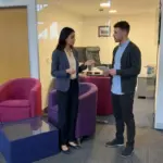 Two colleagues discuss website page planning in an office while reviewing notes together.