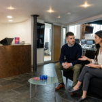 Two colleagues consult on SEO planning in a modern office, seated on a sofa and discussing notes.