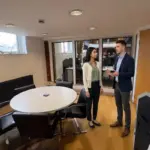 Two colleagues discuss a small business marketing plan in a UK office while standing on open floor space.