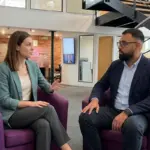 Two colleagues sit in a modern office discussing an AI-led marketing workflow.