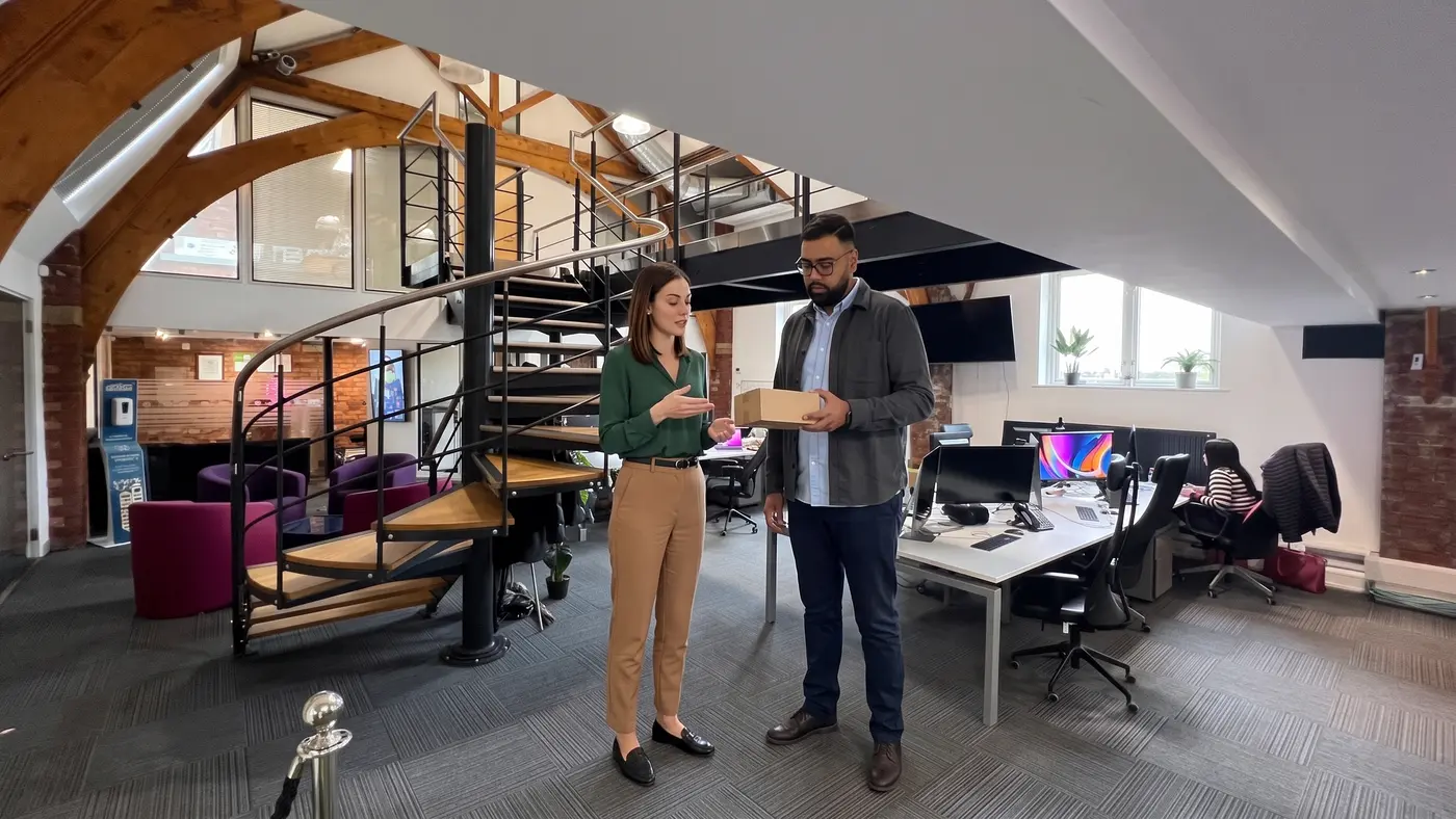 Two colleagues discuss a plain parcel beside desks in a modern office.