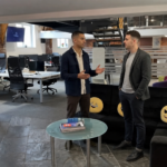 Two colleagues discuss Shopify SEO planning in a UK office while standing in an open workspace.