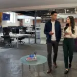 Two colleagues in an office discuss a TikTok content idea while one holds an unreadable phone.