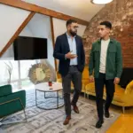 Two colleagues discuss AI search citation strategy while walking through a modern office.