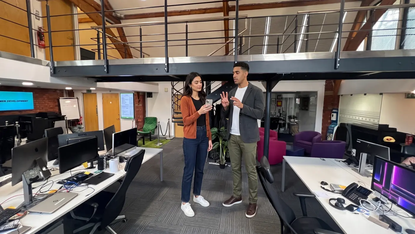 Two colleagues review a phone hook beside green chairs in a bright open-plan office