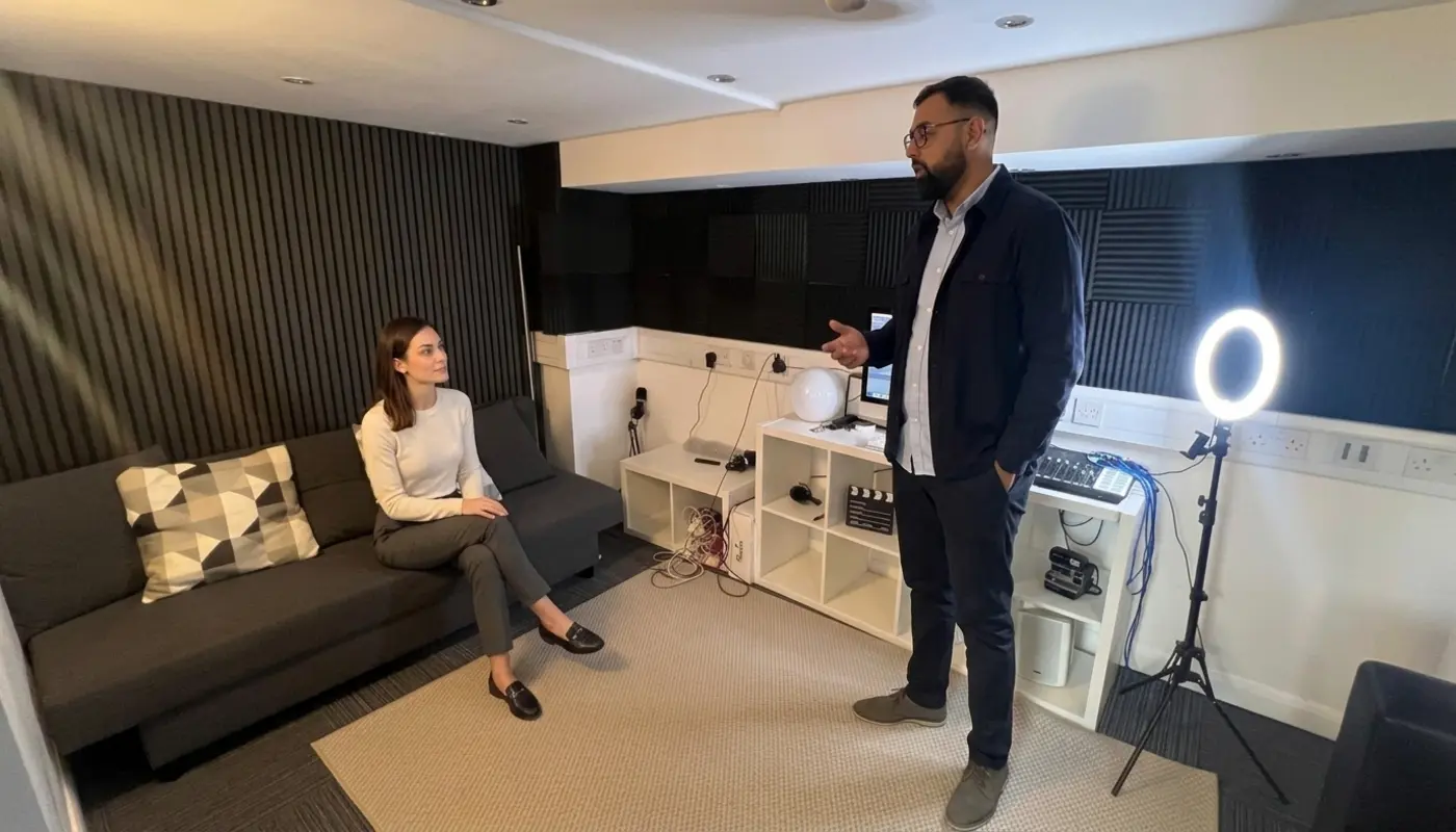 Two colleagues discuss brand lettering in a small office, with one seated on the sofa and one standing nearby.